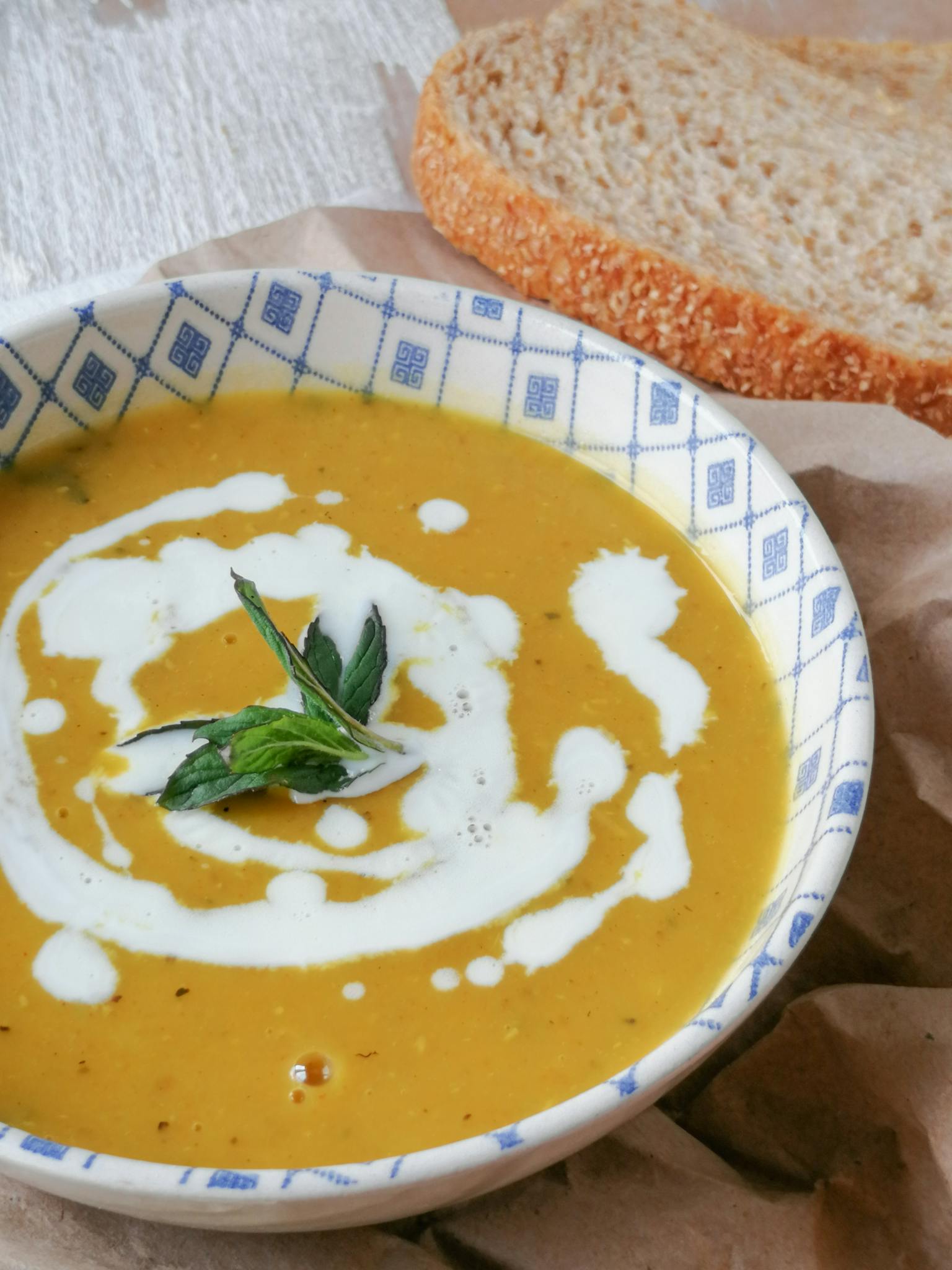 Delicious homemade pumpkin soup topped with herbs and a drizzle of cream, served with bread.