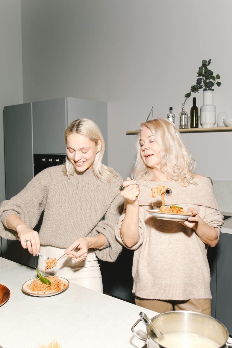 Mother and daughter sharing a joyful meal with spaghetti in a modern kitchen, capturing family togetherness.