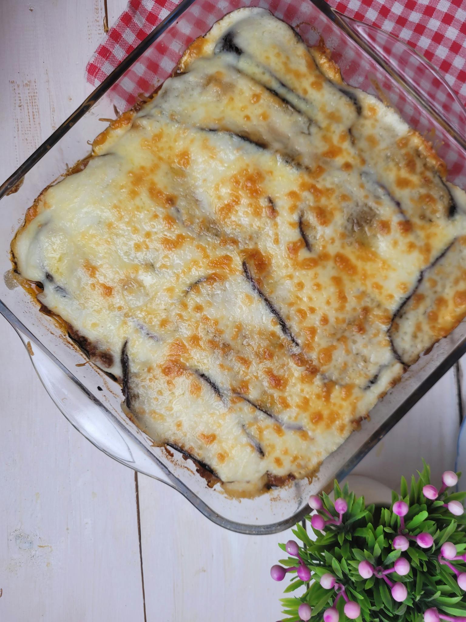 Top view of a golden baked cheese and eggplant casserole in a glass dish.